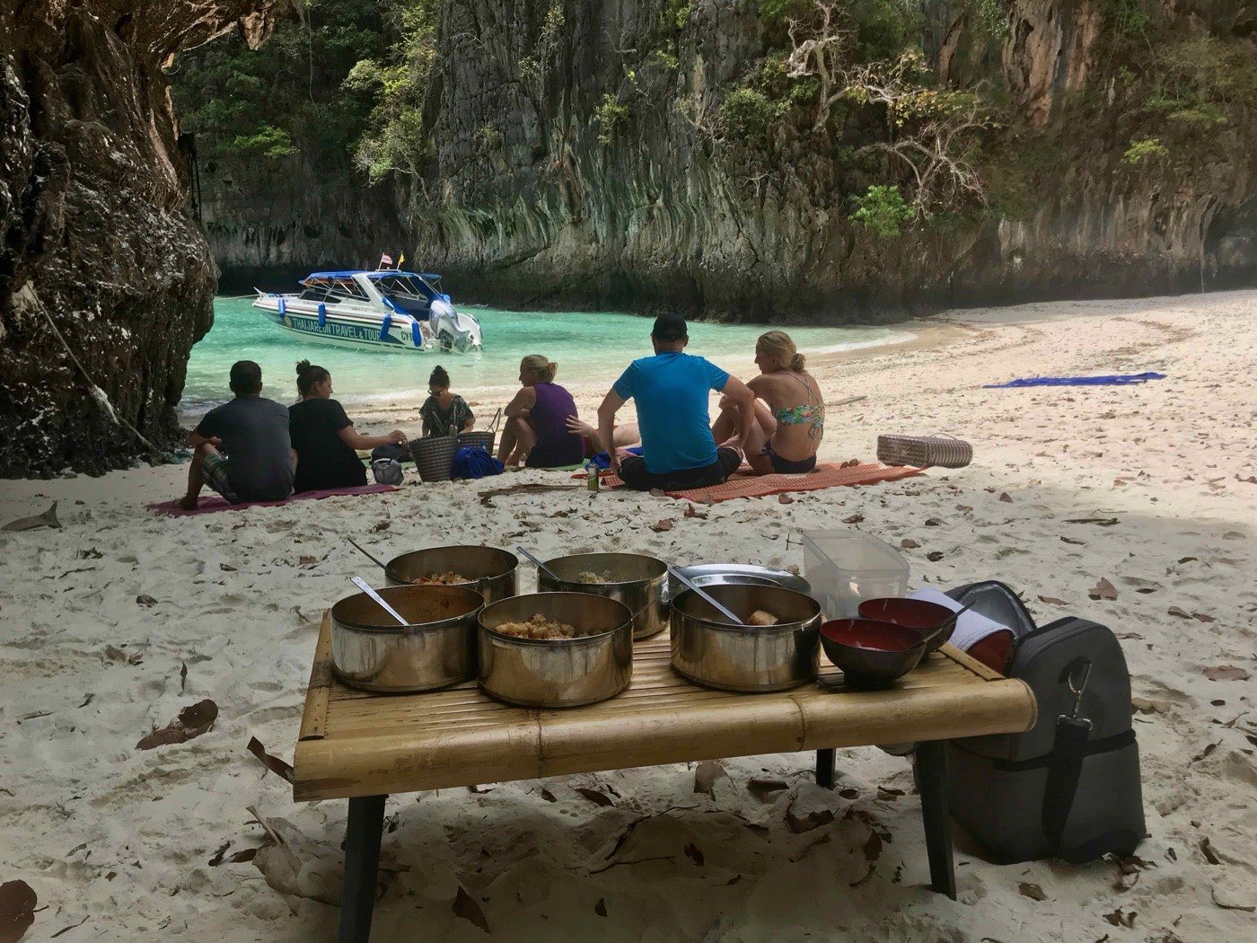 Des voyageurs partagent un repas thaï sur une plage vide, un bateau au mouillage